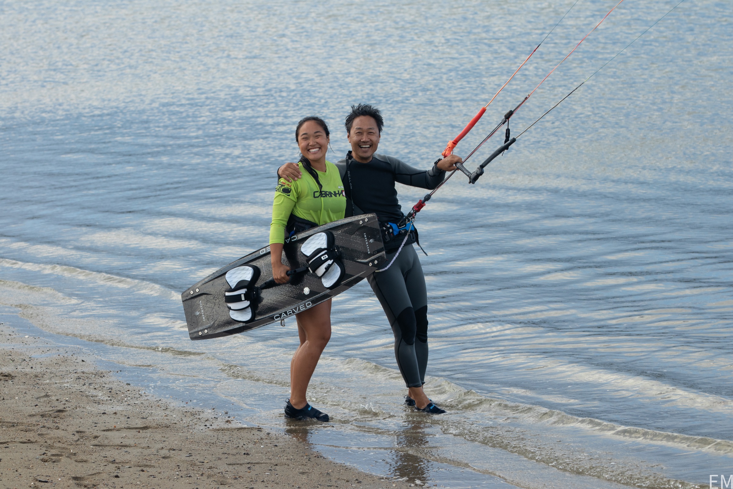 Two kiteboarders smiling together at the water's edge
